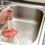 Man holding a plunger with one hand and water in sink